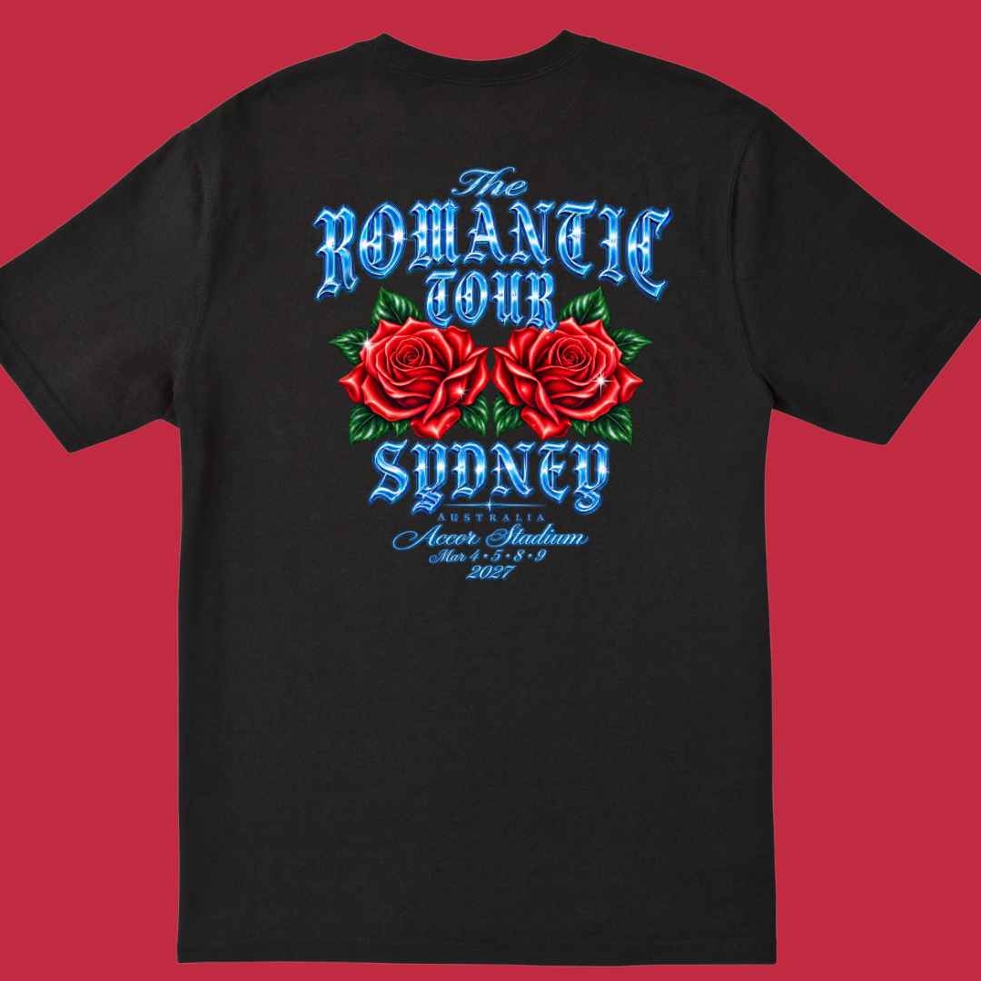 A black short-sleeve t-shirt shown flat against a solid red background, featuring a large graphic print on the back with two red roses, green leaves, and blue gothic-style text reading 'The Romantic Tour Sydney' and 'Accor Stadium'.